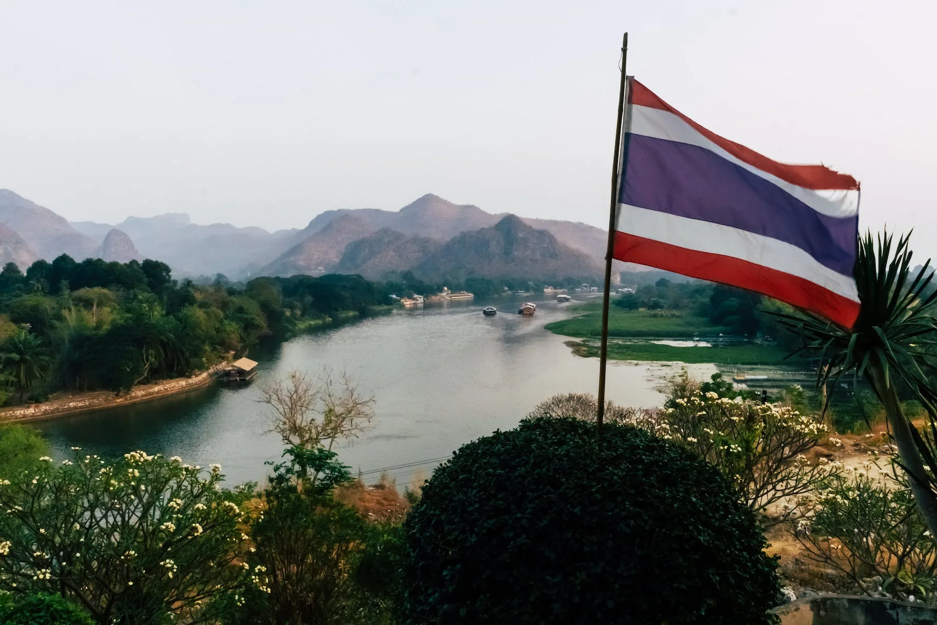 mountain and river landscape behind thailand flag